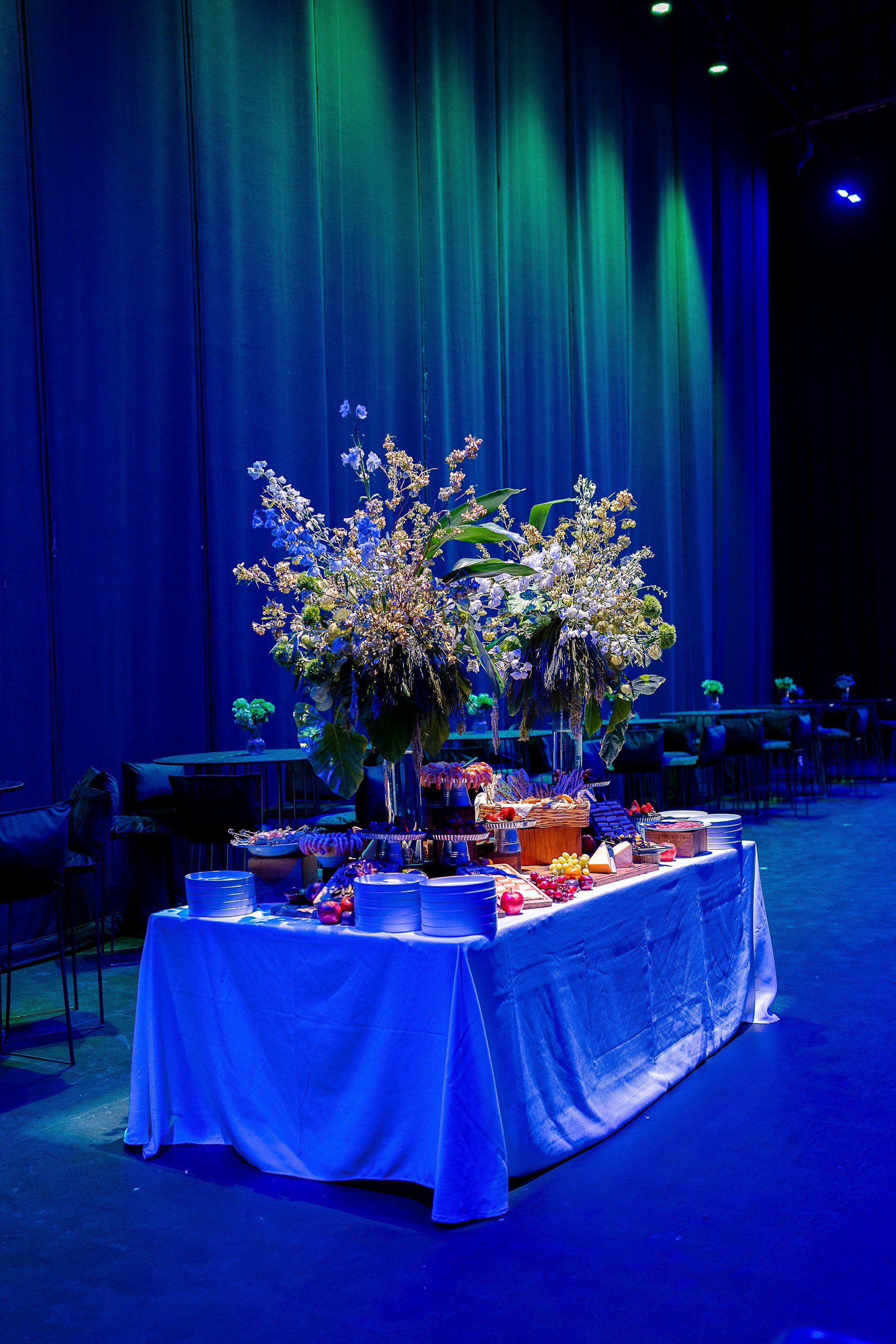 Blue-lit stage display featuring a white flowering arrangement and decorative items on a draped table under atmospheric green lighting