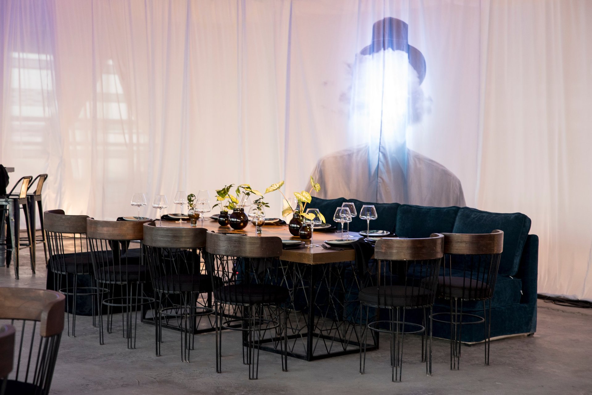 Modern dining space with curved wooden table, black metal chairs, and projected light art on sheer white wall backdrop