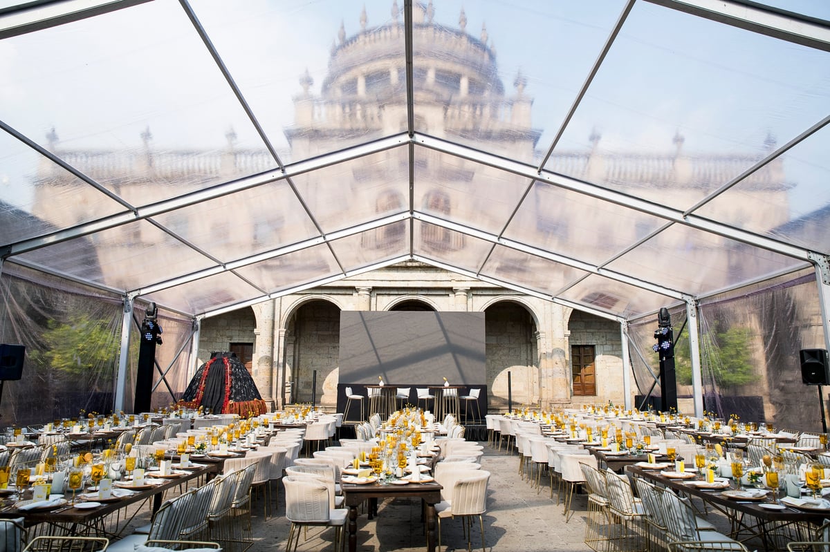 Clear-roofed event tent with long dining tables set for a formal dinner, historic domed building visible in background