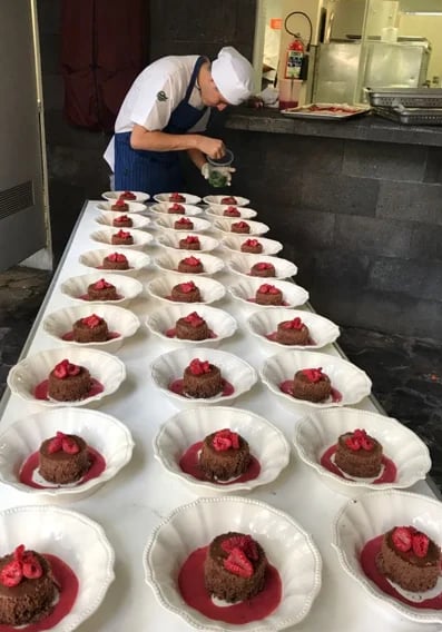Chef plating chocolate desserts with raspberry sauce on white plates in a commercial kitchen