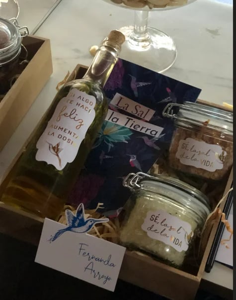 Gift box containing a bottle of olive oil with custom label, artisanal jars, and handwritten name cards labeled Fernanda Arruego