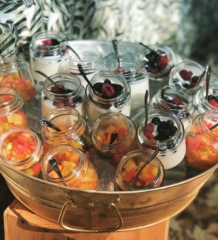 Mason jars with fruit drinks and berries in a metal tub on a wooden table outdoors